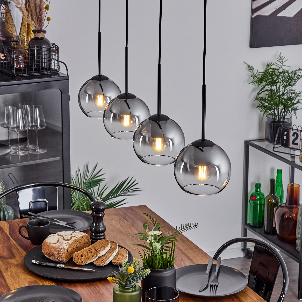 Ein Esszimmer mit einem Holztisch und vier Pendelleuchten mit silbernen Kugelleuchten. Es gibt einen schwarzen Schrank und andere Dekorationen.