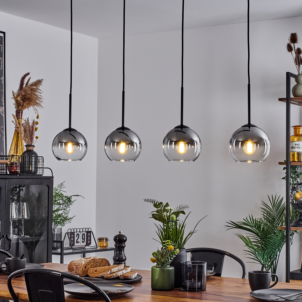 Esszimmer mit vier hängenden Pendelleuchten. Holztisch, Pflanzen und Dekoration. Weiches Licht und neutrale Töne.