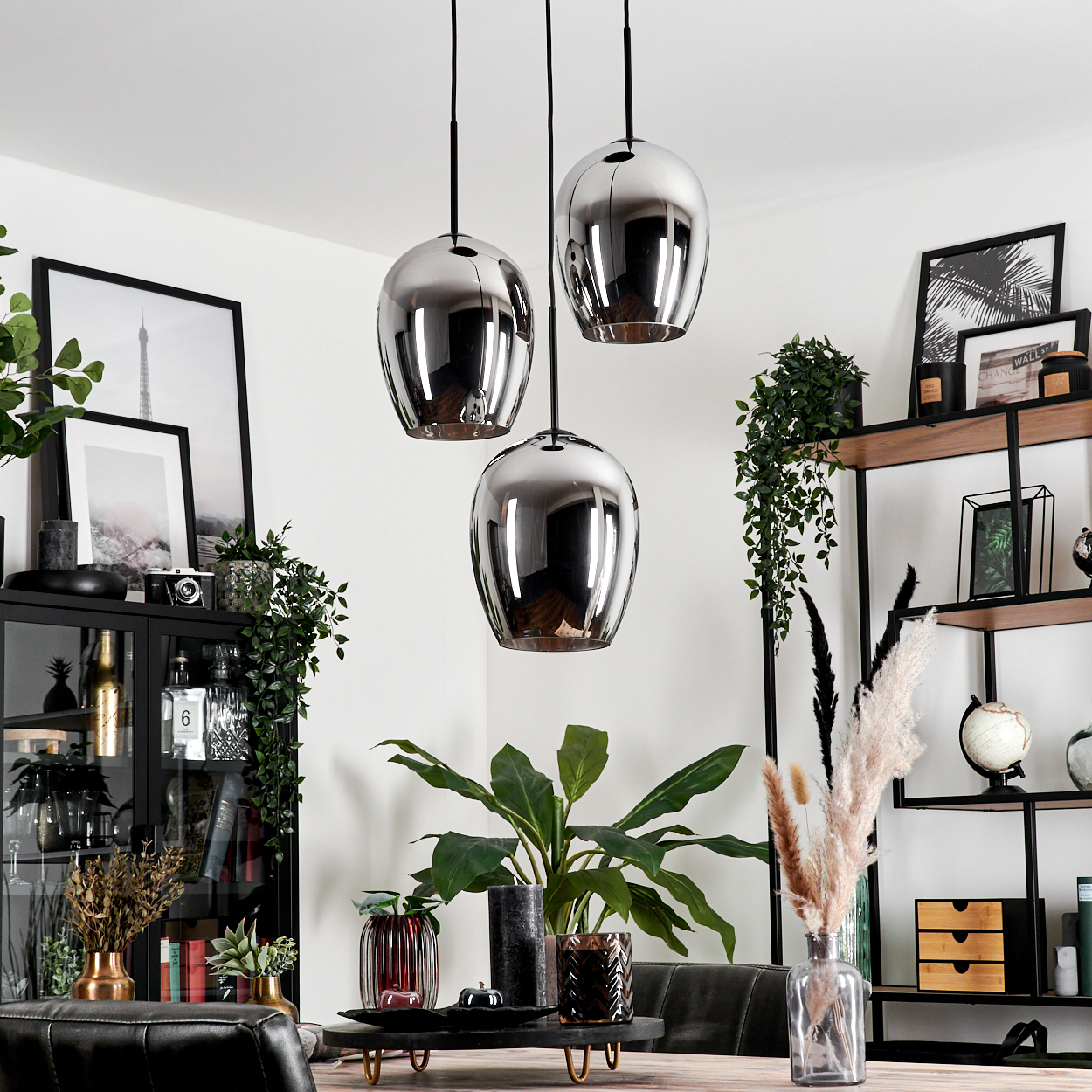 Wohnzimmer mit drei Pendelleuchten. Pflanzen, Bücher und Dekoration. Spiegelähnliche Pendelleuchte. Warme Töne.
