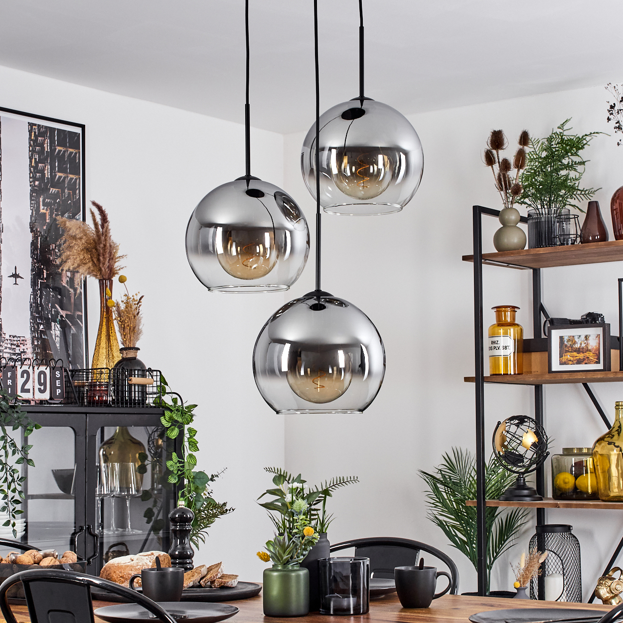 Esszimmer mit drei Pendelleuchten. Holztisch, Dekoration und Pflanzen. Warme Beleuchtung. Gemütliche Szene.