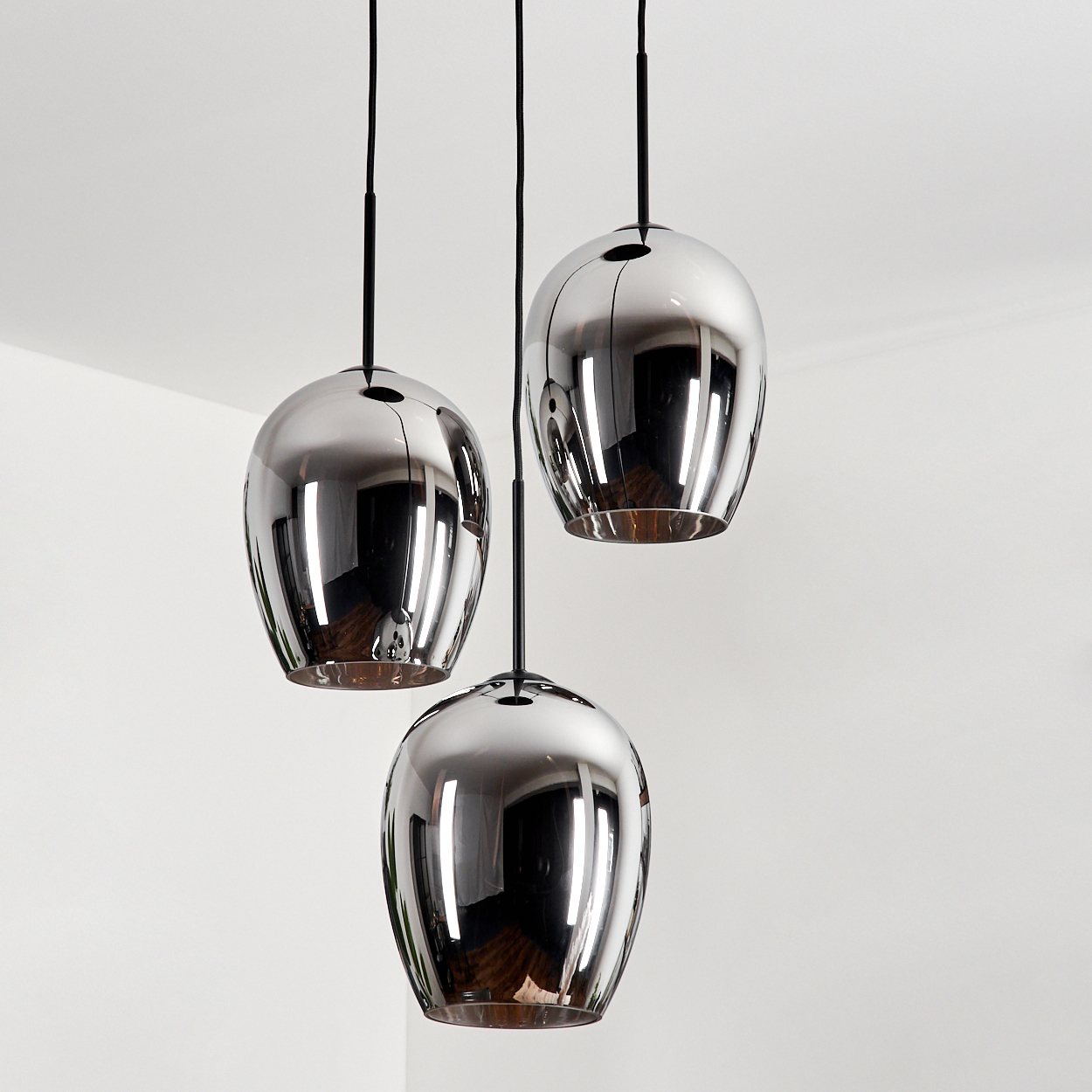 Drei tropfenförmige Chrom-Pendelleuchten hängen in einer Ecke, mit weißem Hintergrund.