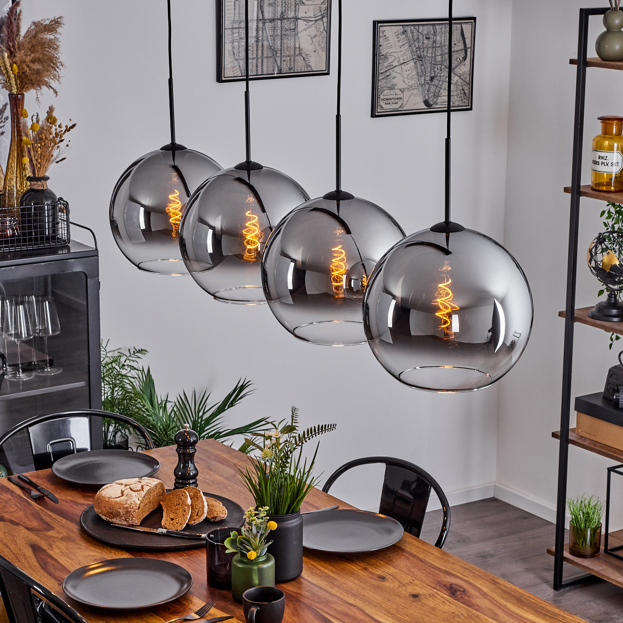 Vier Pendelleuchten mit kugelförmigen, verspiegelten Glasschirmen hängen über einem Holztisch mit Tellern und Essen.