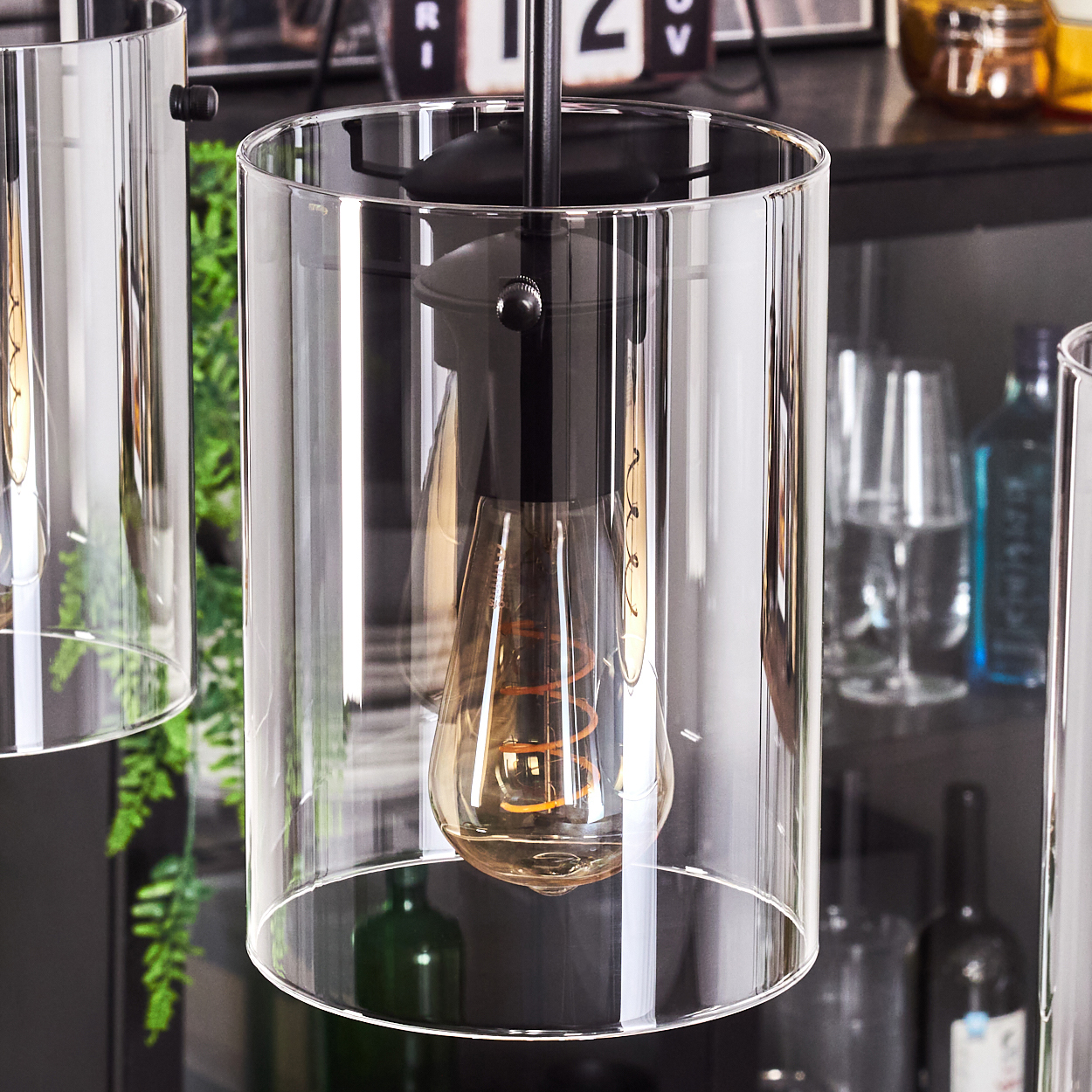 Nahaufnahme von drei Pendelleuchten mit zylindrischen, klaren Glasschirmen und Edison-Glühbirnen.