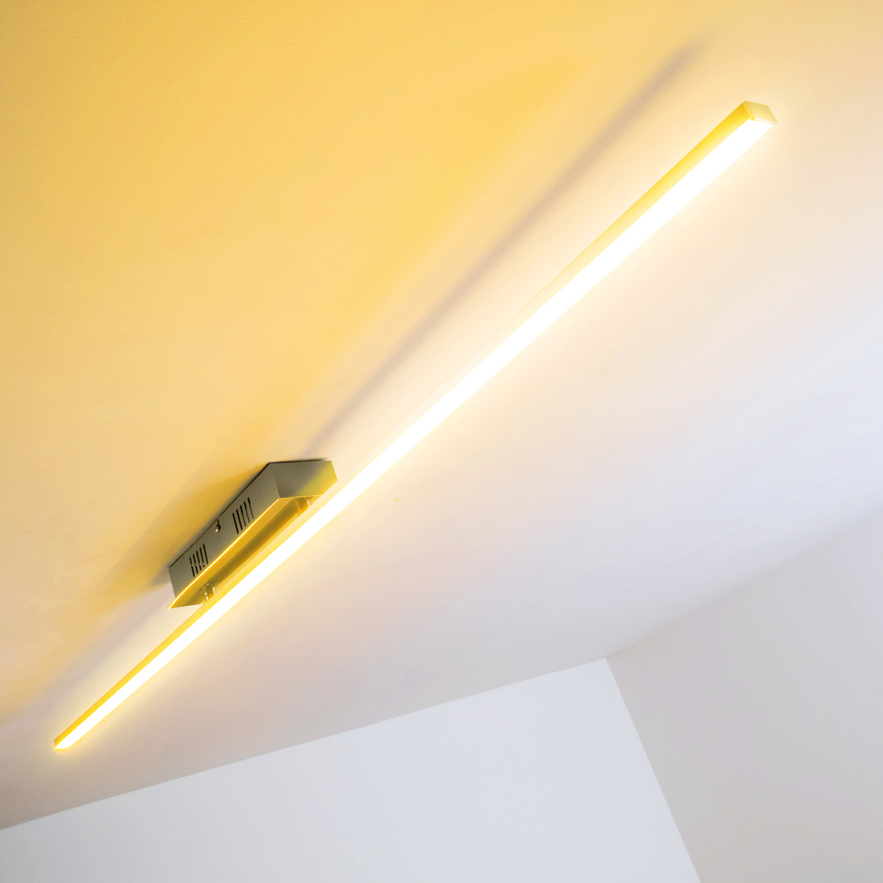 Eine lange, beleuchtete LED-Leuchte ist an einer weißen Decke montiert. Sie strahlt warmes Gelb aus.