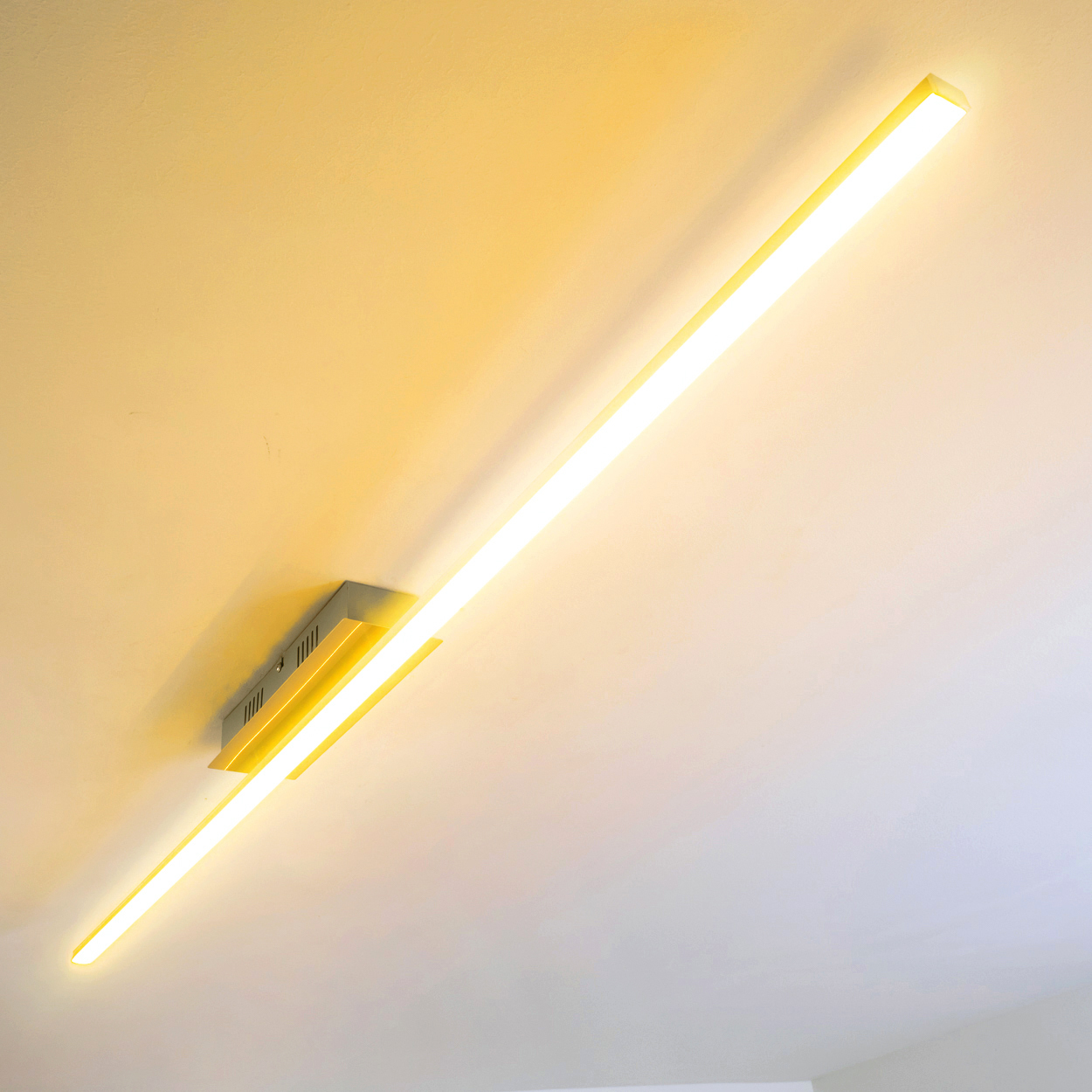 Eine lange, beleuchtete LED-Leuchte ist an einer weißen Decke montiert. Sie strahlt warmes Gelb aus.