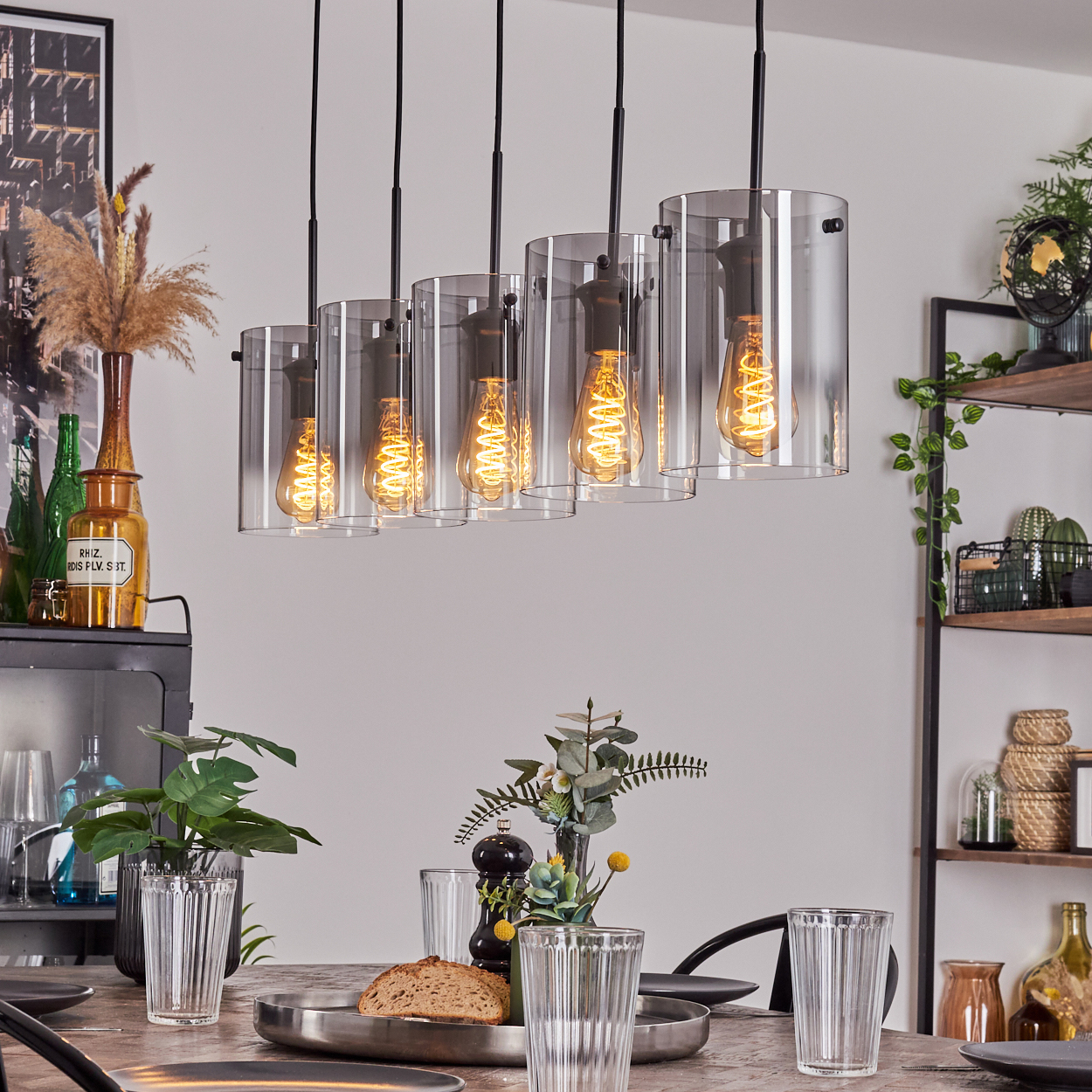 Esszimmer mit Pendelleuchten mit Glasschirmen und Wendelbirnen. Tisch mit Gläsern und Brot gedeckt.