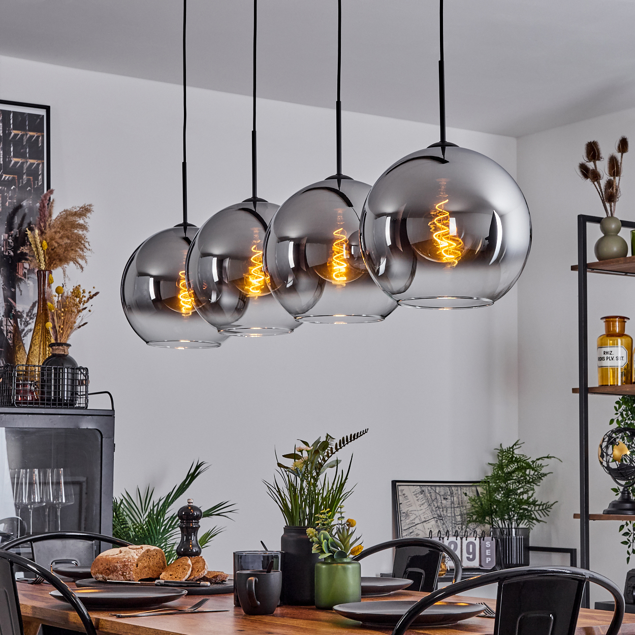 Esszimmer mit Pendelleuchten mit silbernen Kugeln und Wendelbirnen. Tisch mit Gläsern und Brot gedeckt.