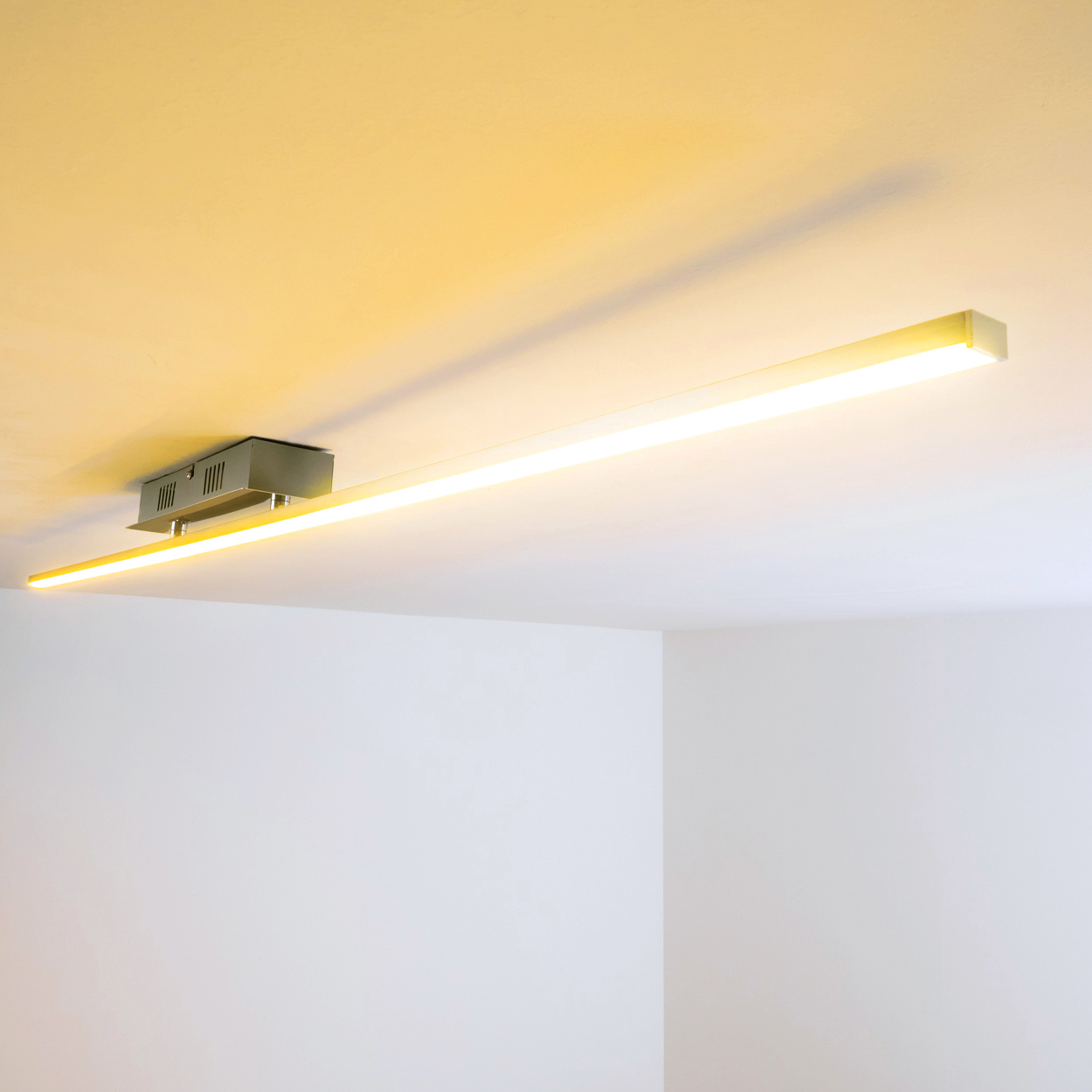 Eine lineare LED-Leuchte an einer weißen Decke, die ein warmes gelbes Leuchten wirft.