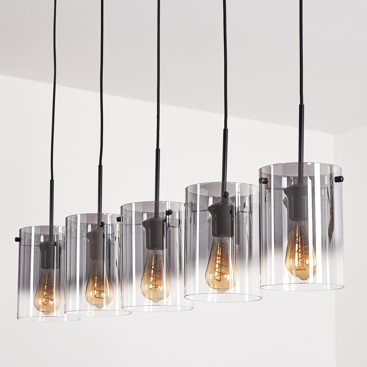 Fünf Pendelleuchten mit zylindrischen Glasschirmen und Edison-Glühbirnen, die von der Decke hängen.