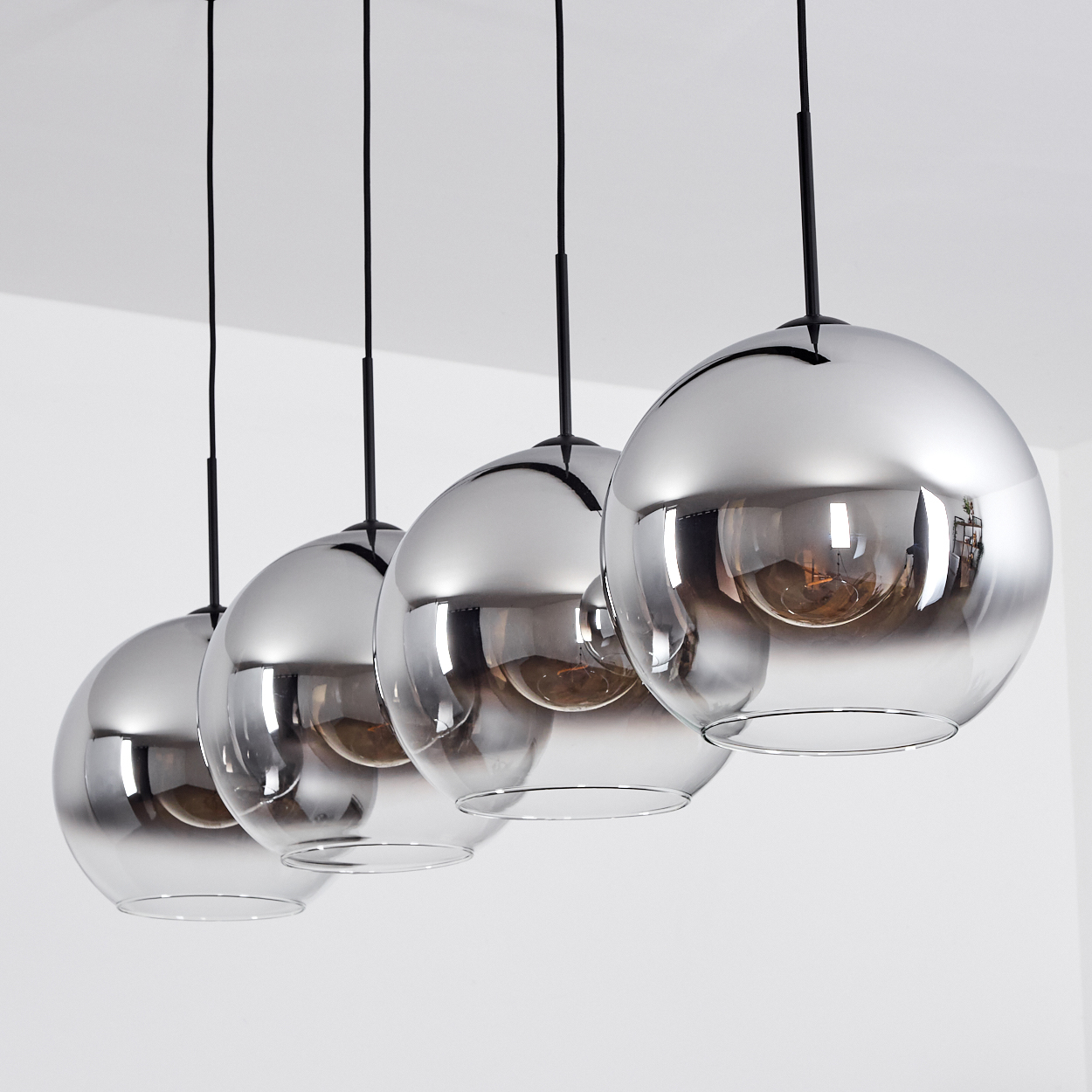 Vier kugelförmige Pendelleuchten mit verspiegelten Glasschirmen, die von der Decke hängen.