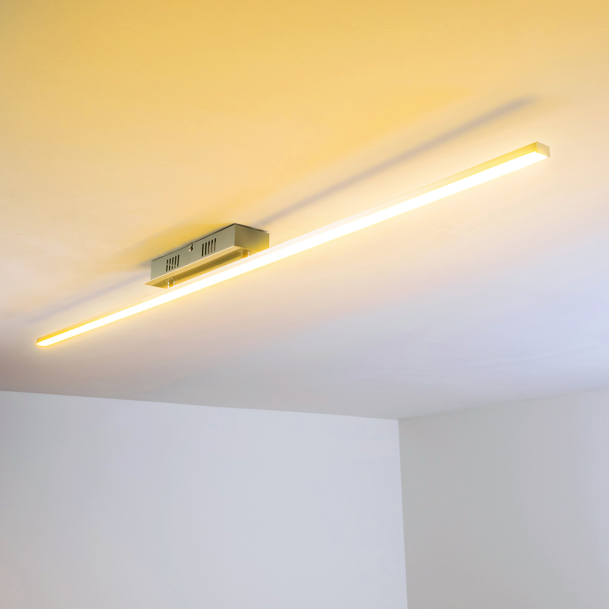 Eine lineare Leuchte an einer weißen Decke, die ein warmes gelbes Leuchten wirft.
