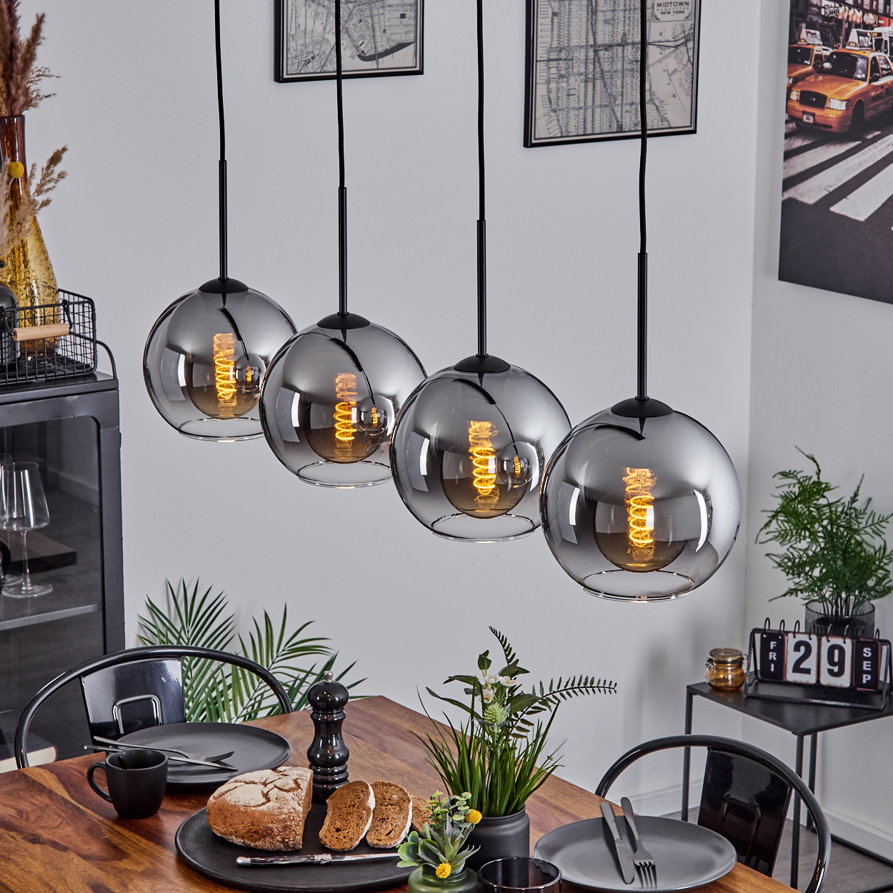 Esszimmer mit vier verspiegelten Pendelleuchten über einem Holztisch, mit Dekoration.