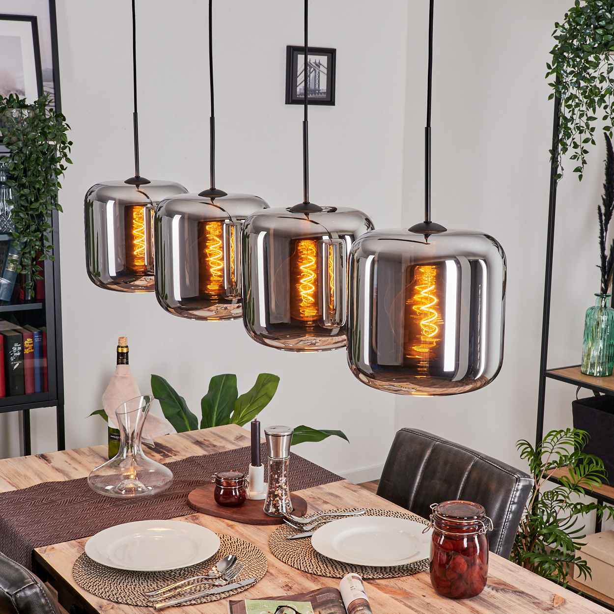 Esszimmer mit Tisch, Pendelleuchten mit Spiralglühbirnen und Pflanzen. Eine Glaskaraffe ist sichtbar.