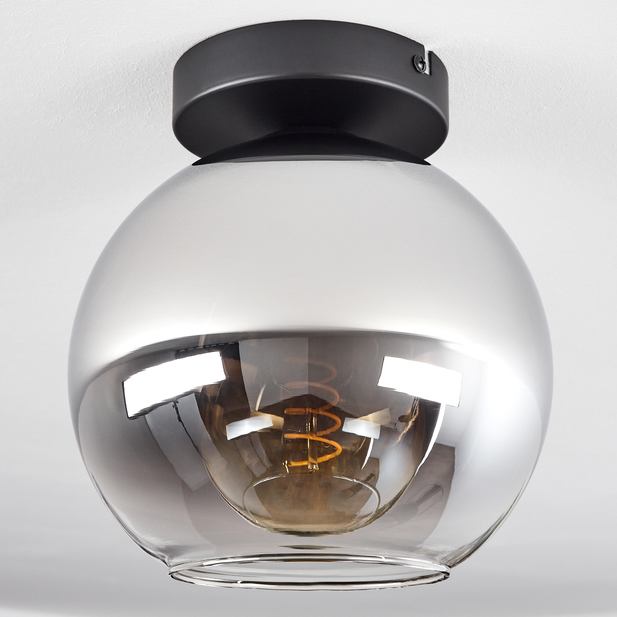 Eine runde Glaslampe mit sichtbarer Glühbirne, montiert an einer weißen Decke. Die Lampe hat einen schwarzen Sockel.