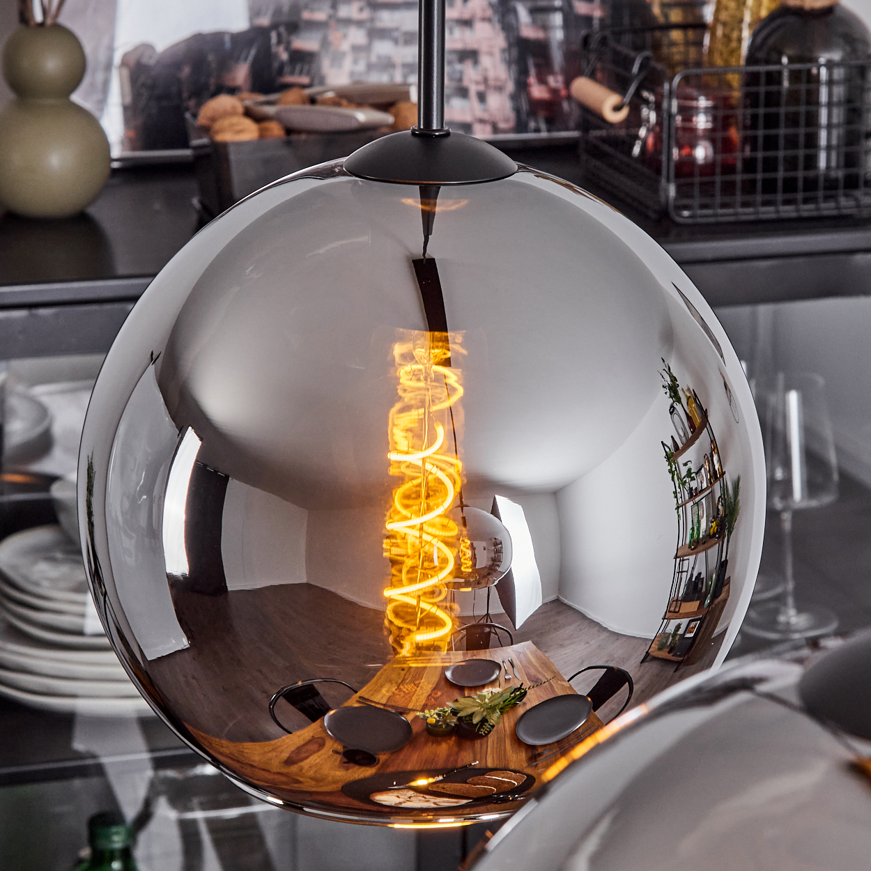 Eine Pendelleuchte mit kugelförmigem Schirm. Die Glühbirne ist sichtbar und der Hintergrund ist ein Esszimmer.