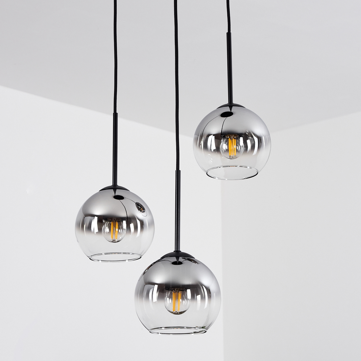 Drei Pendelleuchten mit Chromkugelschirmen hängen an schwarzen Schnüren. Die Lichter reflektieren das Innere des Raumes.