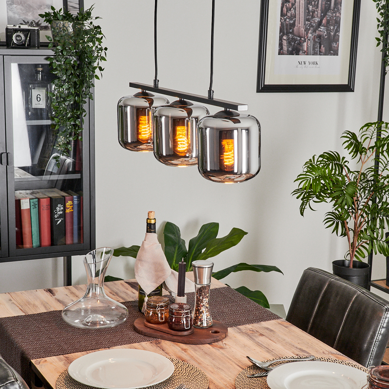 Ein Esszimmer mit einem Holztisch, drei Hängelampen und Dekoration. Enthält eine Weinflasche und andere Gegenstände.