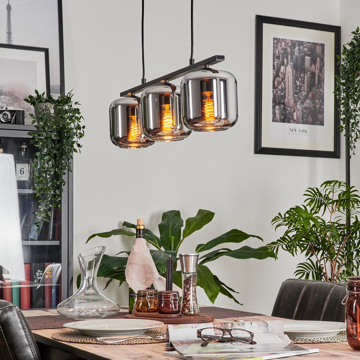 Ein Esszimmer mit gedecktem Tisch und drei Pendelleuchten. Die Lichter beleuchten die Tischdekoration.