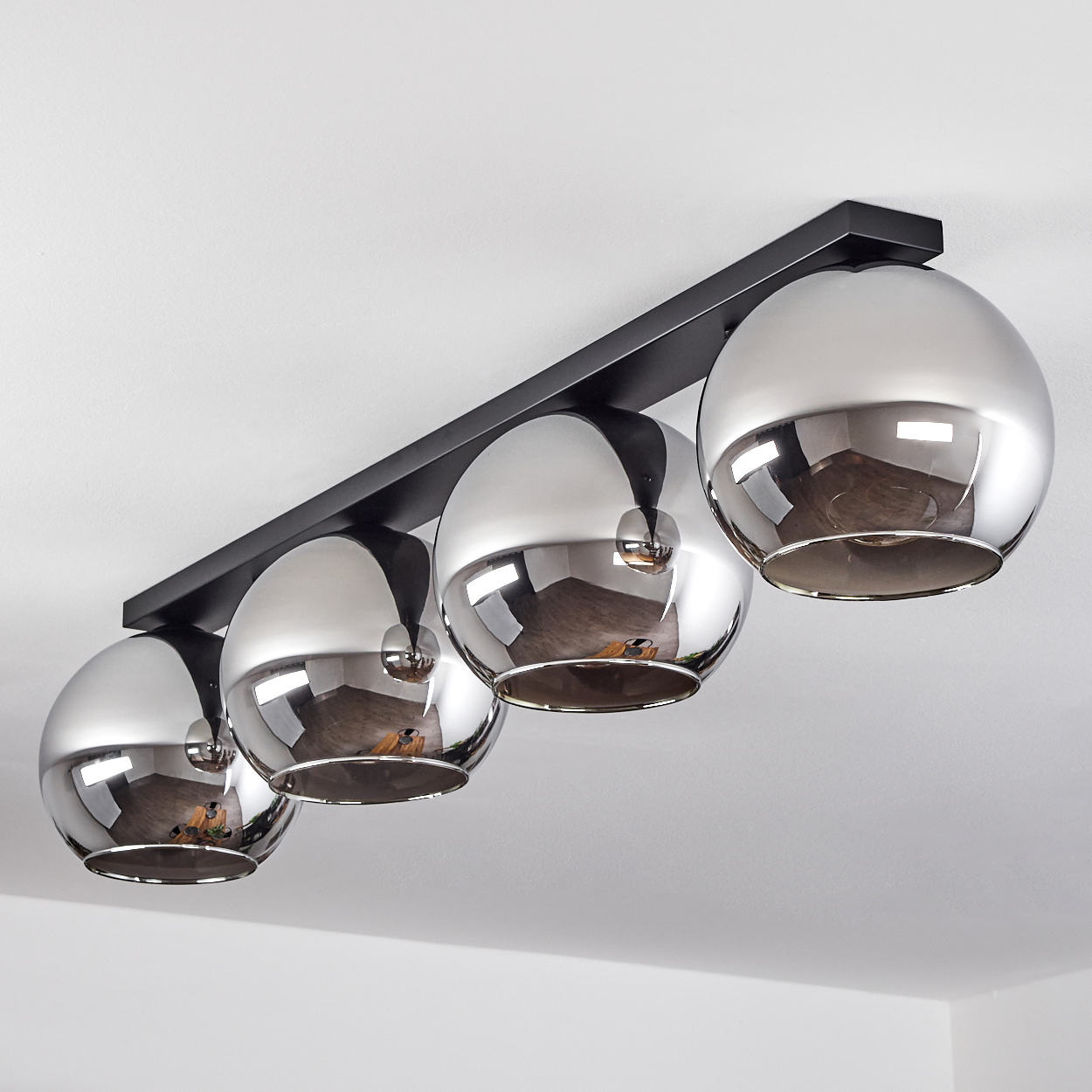 Vier Chrom-Kugel-Leuchten an einer schwarzen rechteckigen Stange, an einer weißen Decke befestigt.