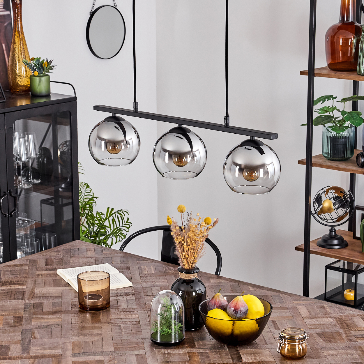 Esszimmer mit Holztisch und drei Pendelleuchten. Verschiedene Objekte sind angeordnet.