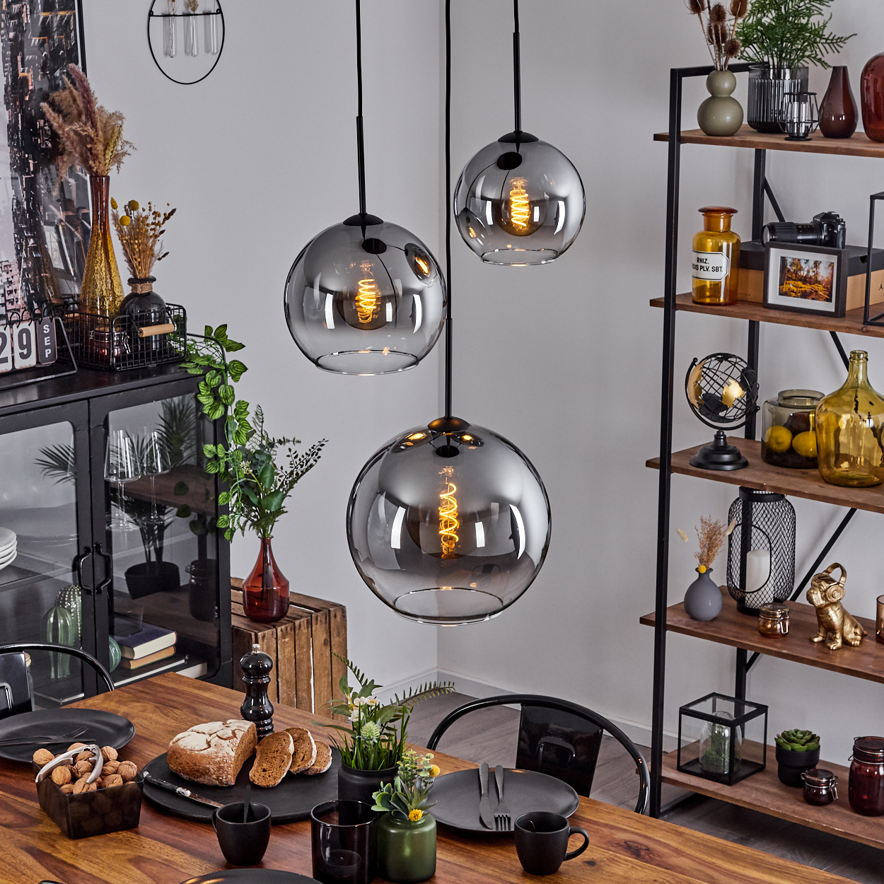 Esszimmer mit Holztisch, drei kugelförmigen Pendelleuchten und dekorativen Gegenständen.