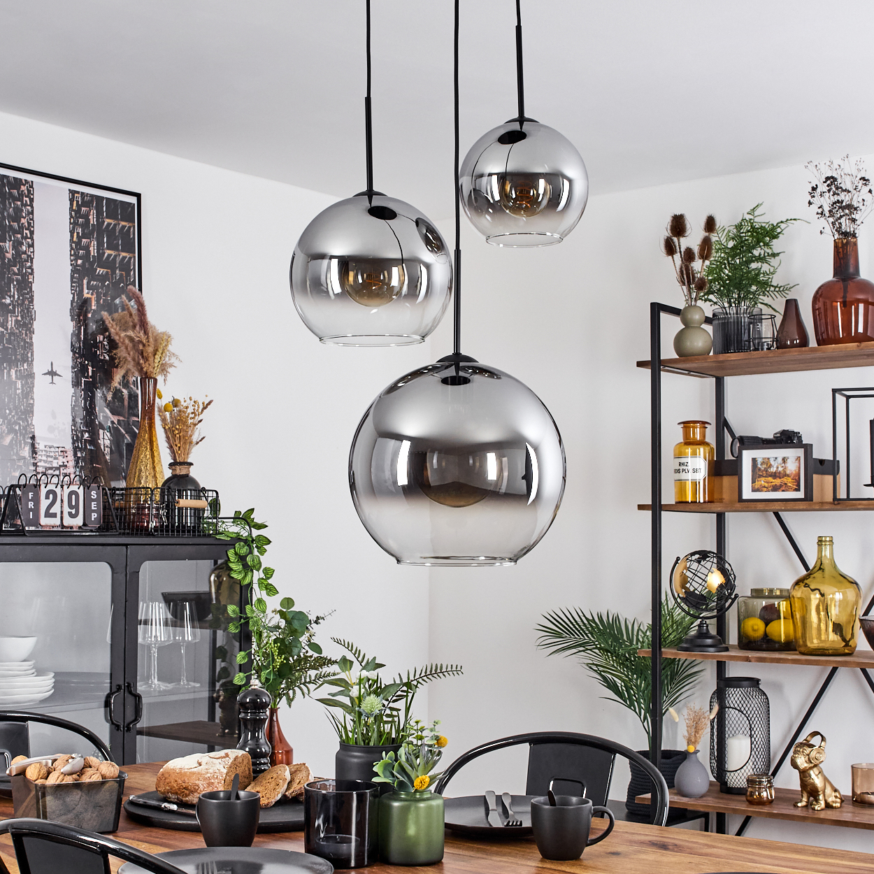 Esszimmer mit Holztisch, drei kugelförmigen Pendelleuchten und dekorativen Gegenständen.
