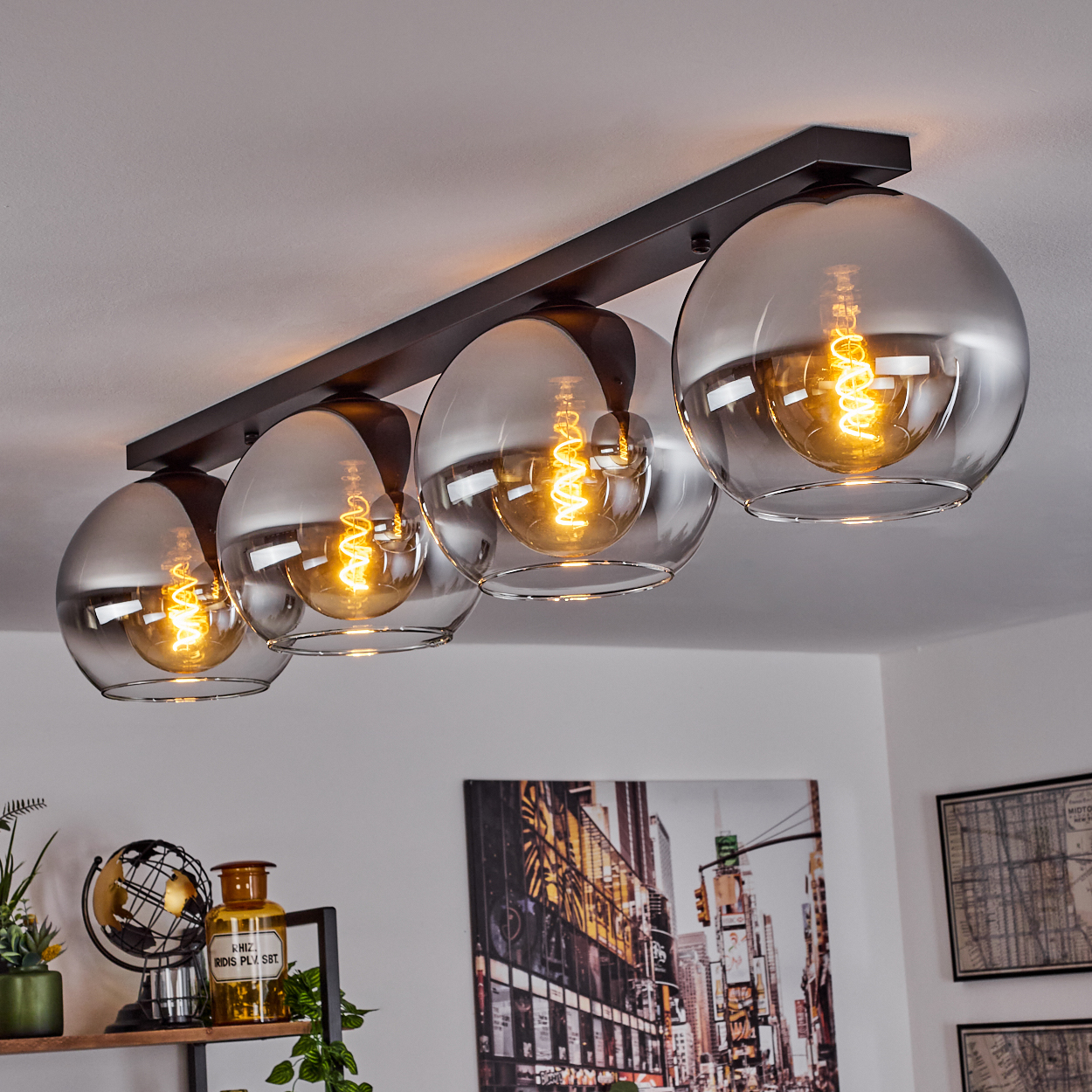 Vier kugelförmige Pendelleuchten an einer dunklen Metallstange, mit Globus und gerahmtem Bild.