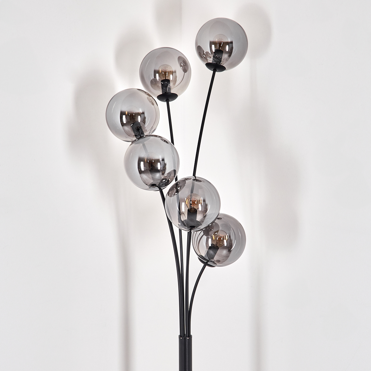 Eine Stehlampe mit sechs silbernen Kugelleuchten an schwarzen Stielen. Der Hintergrund ist eine weiße Wand.