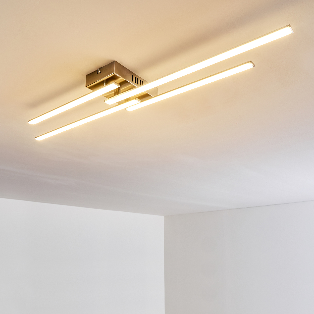 Deckenleuchte mit drei rechteckigen Lichtbalken, die warmes Licht aussenden. Die Leuchte ist metallisch, die Decke ist weiß.