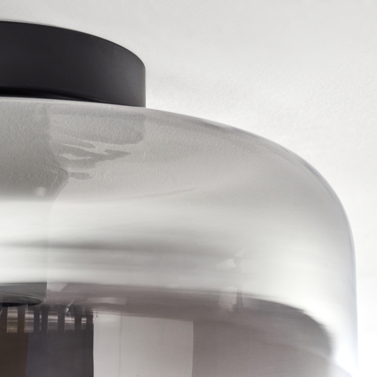 Nahaufnahme einer Deckenleuchte. Das Glas ist rauchig, die Glühbirne leicht sichtbar. Oben ein schwarzer Deckel.