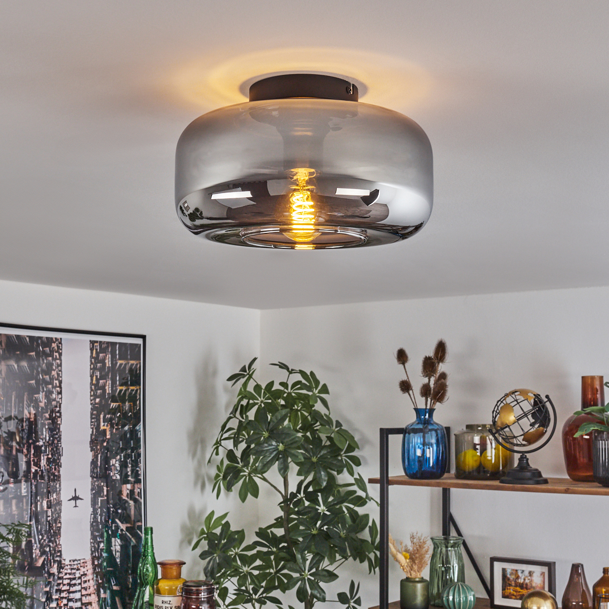 Deckenleuchte mit Chromoberfläche und sichtbarer Glühbirne. Das Licht befindet sich über einem Regal mit Dekor.
