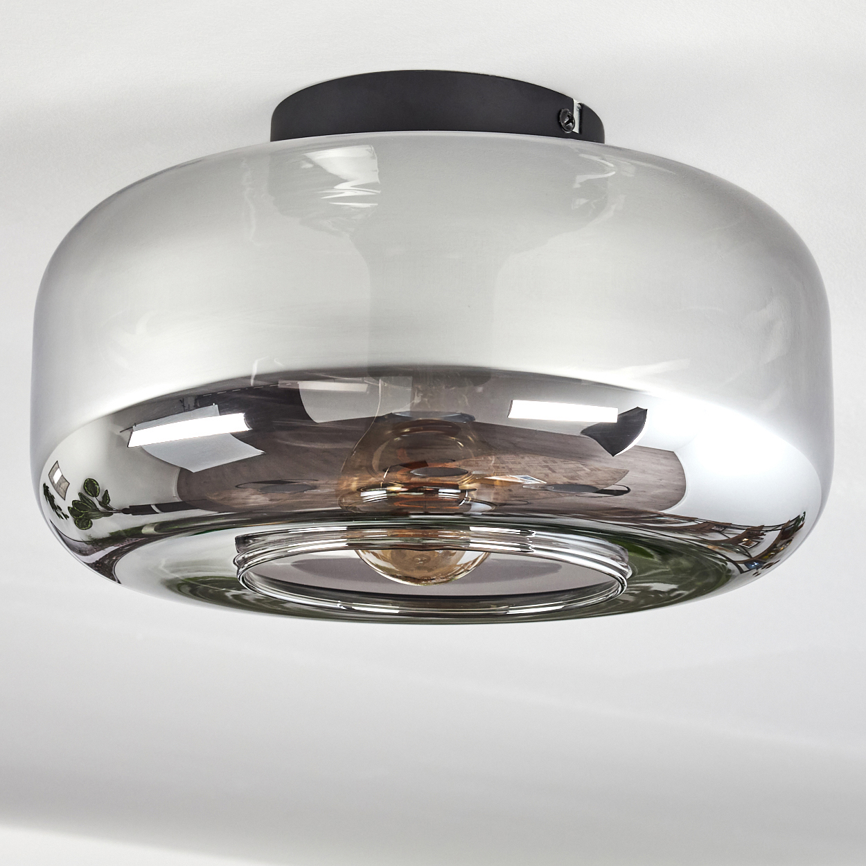 Nahaufnahme einer Deckenlampe mit rundem, reflektierendem Glasschirm und sichtbarer Glühbirne.