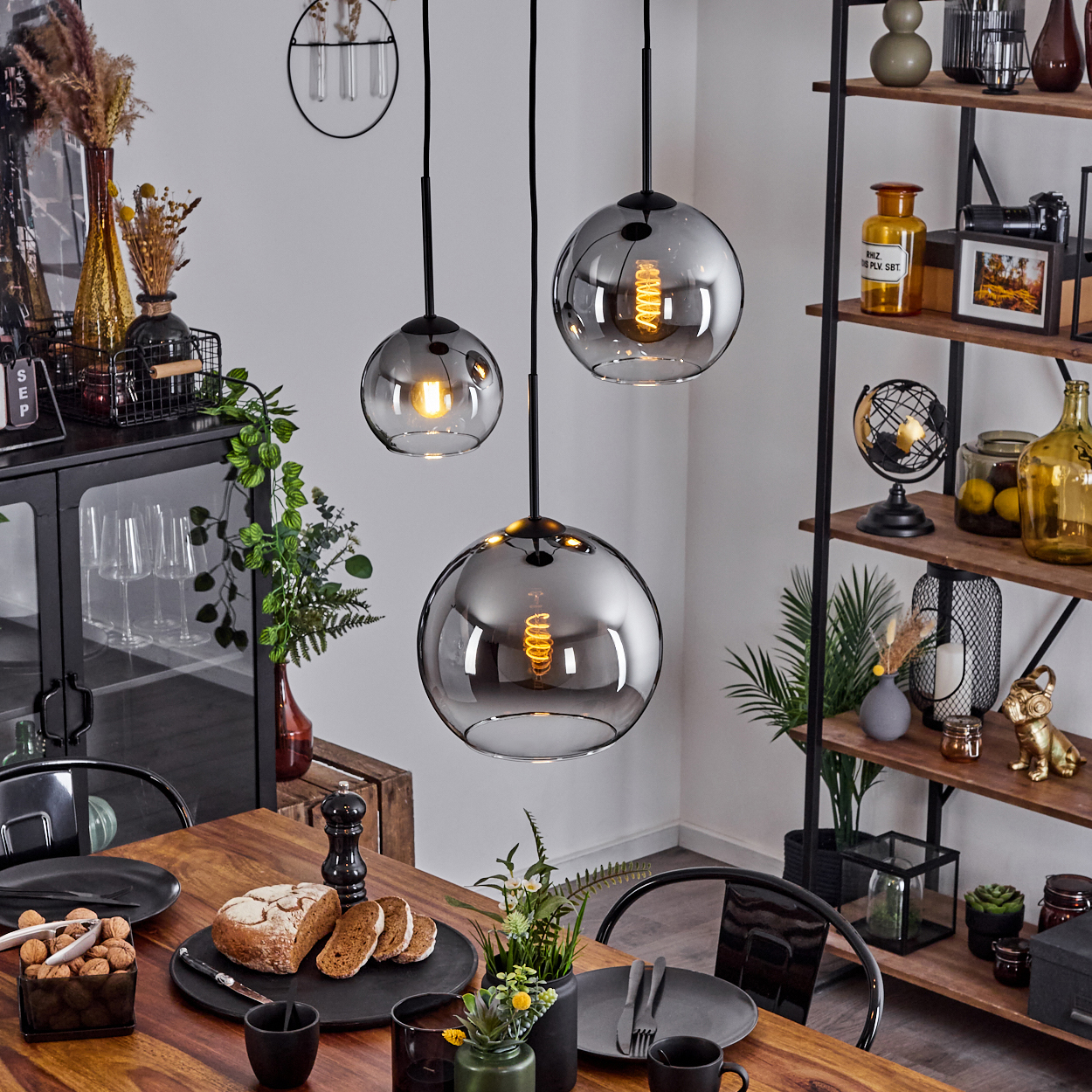 Esszimmer mit drei Pendelleuchten, einem Holztisch und Dekorationsgegenständen auf einem Regal.