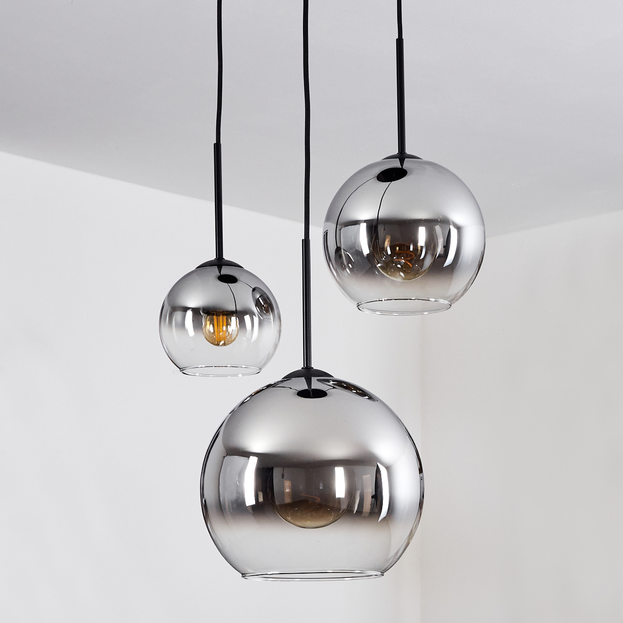 Drei Hängelampen mit Glaskugeln. Jede Lampe hat eine Glühbirne und hängt von der Decke.