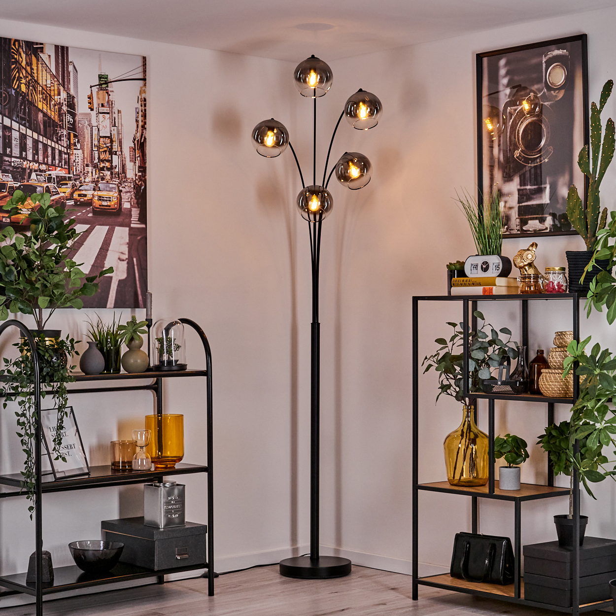 Ein Raum mit Stehlampe, Regalen mit Pflanzen und Stadtbild-Kunstwerk an der Wand.