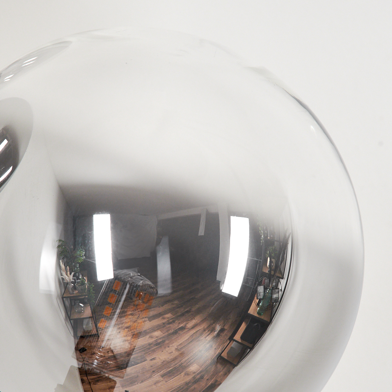 Eine reflektierende Glaskugel, die einen Raum mit Holzboden, Pflanzen und Regalen widerspiegelt.