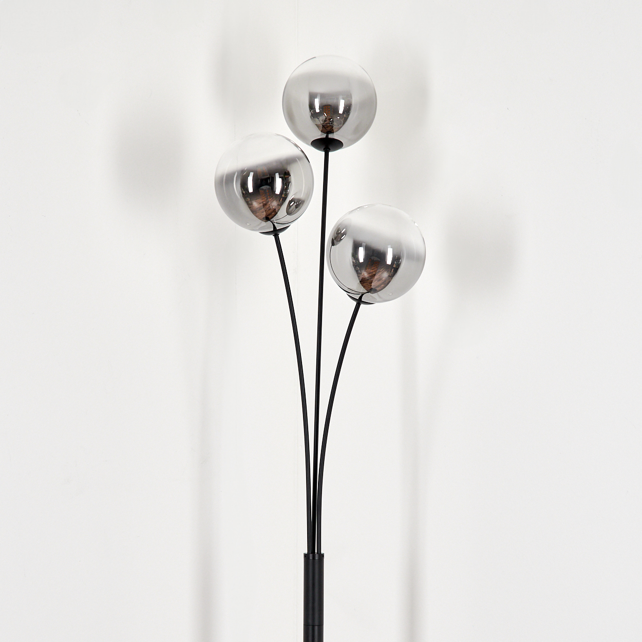 Eine Stehlampe mit drei Kugelleuchten in geschwungenem Design. Der Hintergrund ist schlicht weiß.