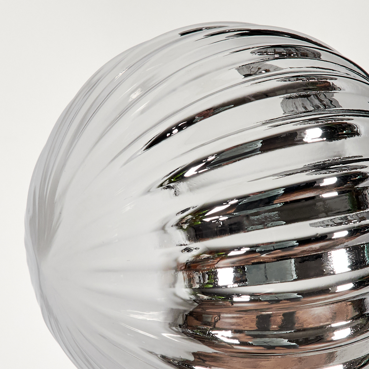 Nahaufnahme einer silbernen, geriffelten Kugel mit reflektierender Oberfläche auf weißem Hintergrund.