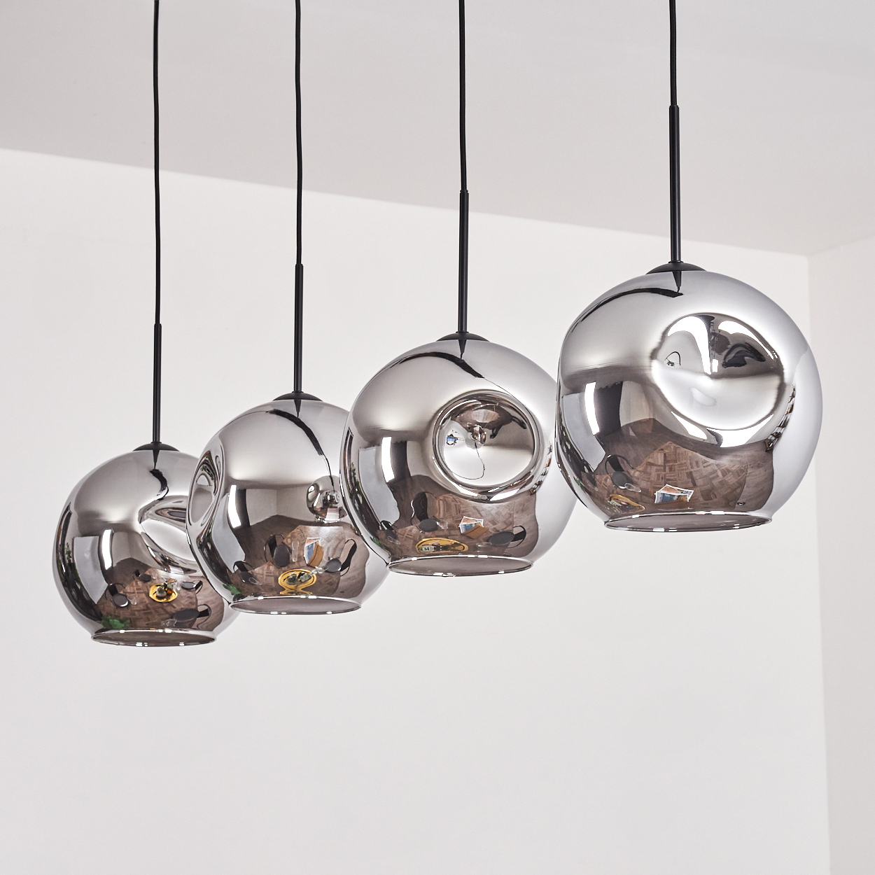Vier silberne, reflektierende Pendelleuchten in einer Reihe hängen. Die Leuchten sind kugelförmig.
