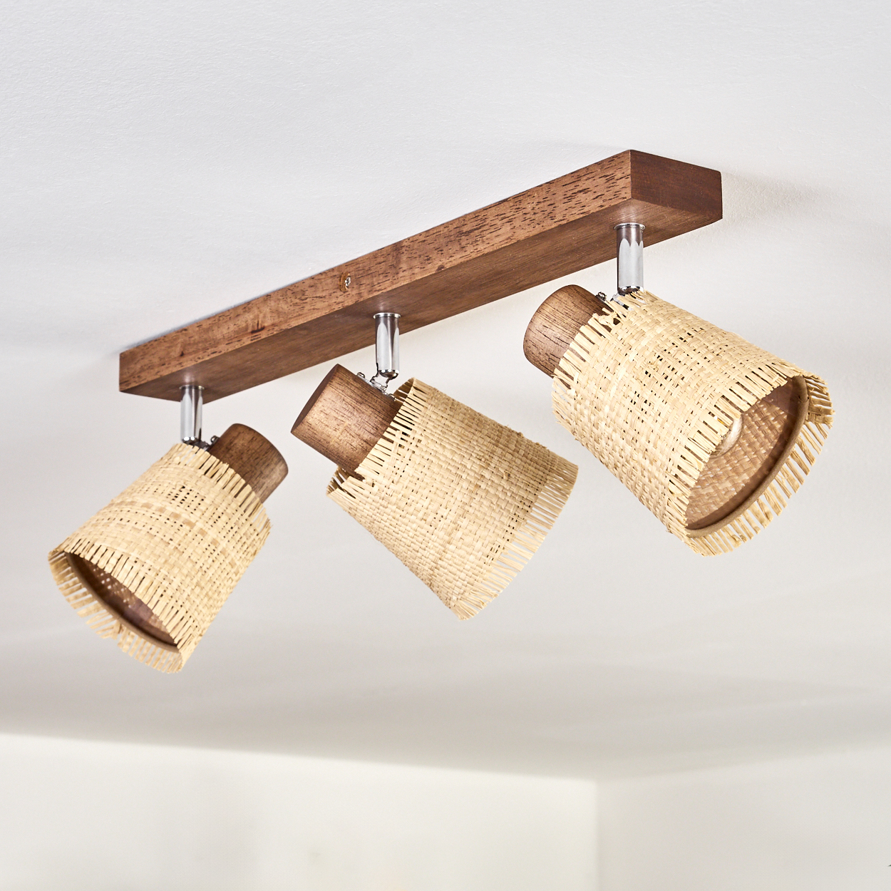 Deckenleuchten mit drei gewebten Lampenschirmen, die an einem Holzbalken befestigt sind. Das Licht ist an.