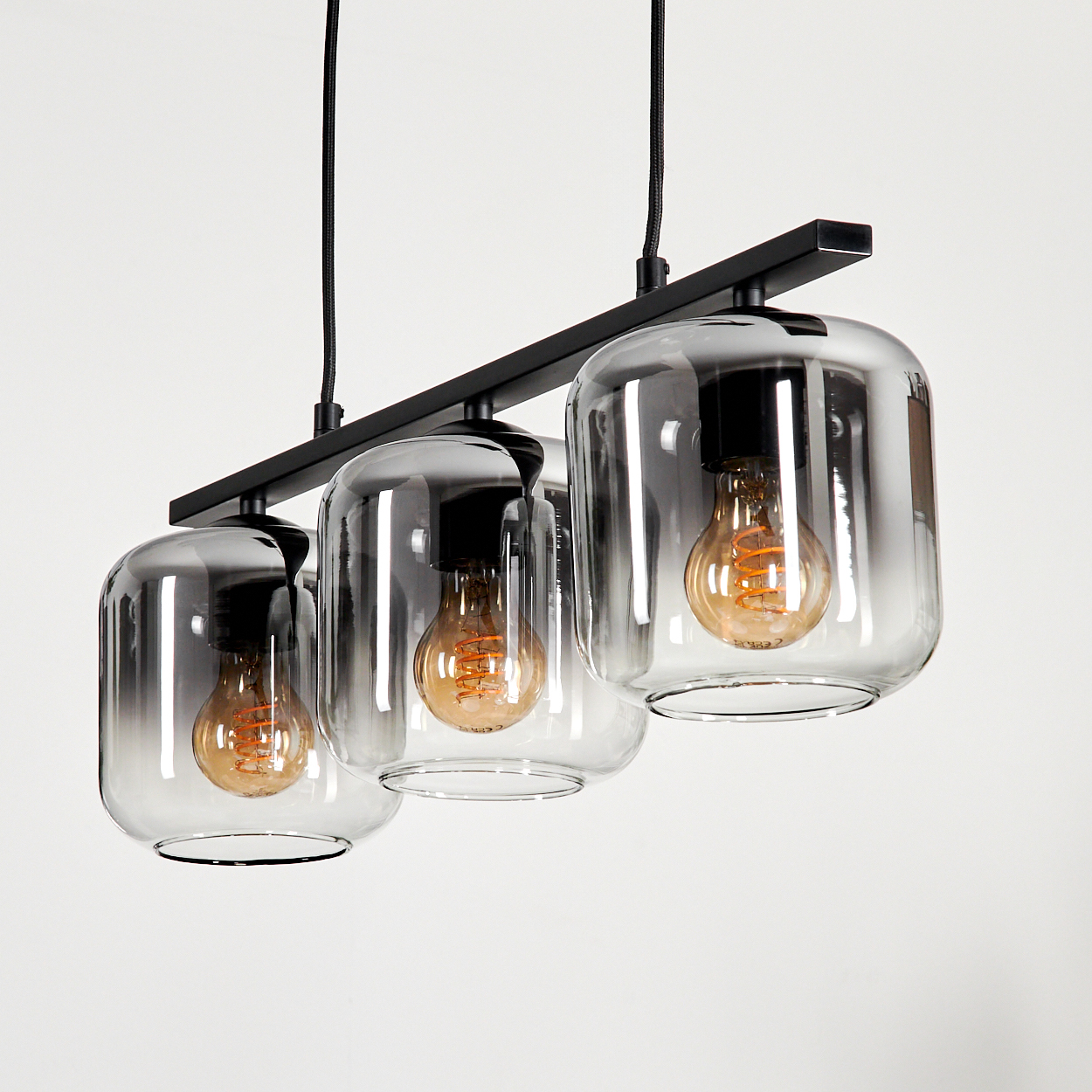 Nahaufnahme einer Pendelleuchte mit drei klaren Glasschirmen und Edison-Glühbirnen auf weißem Hintergrund.