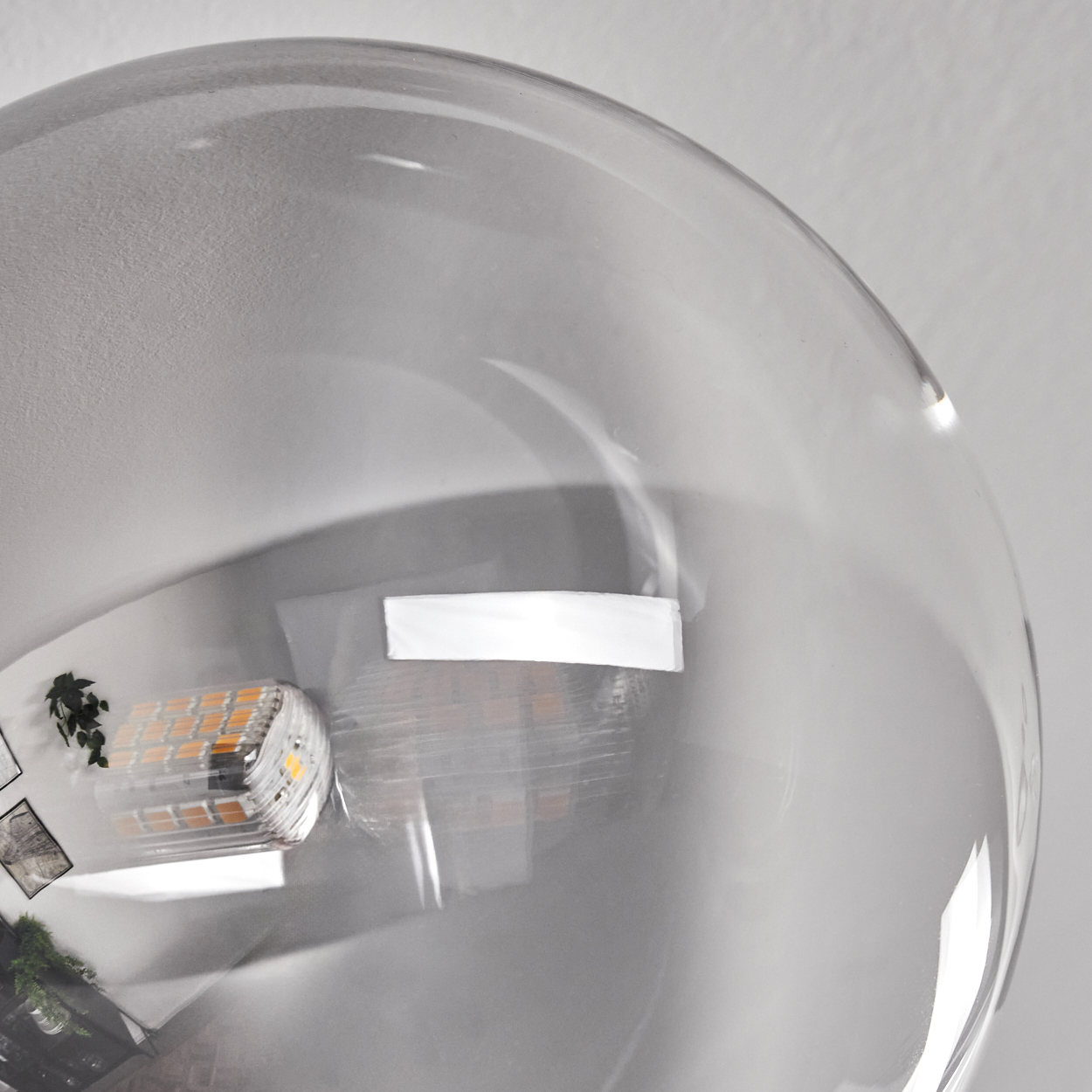 Nahaufnahme einer klaren Glaskugel, die eine Innenszene mit Lichtern und Grün reflektiert.