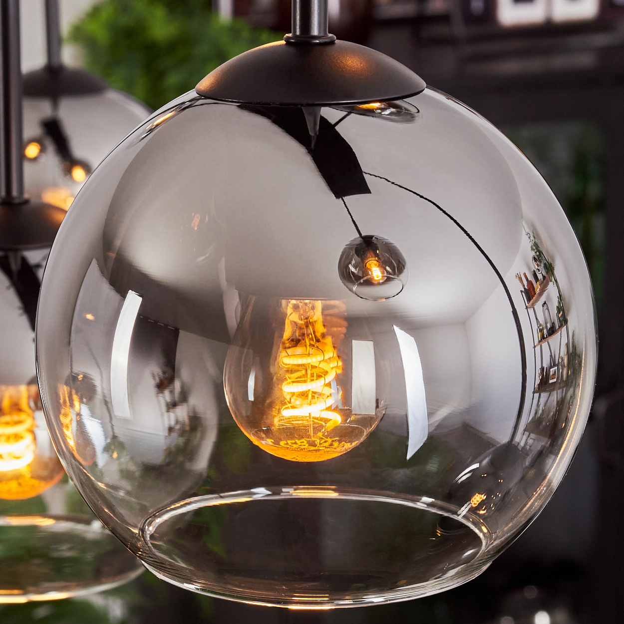 Nahaufnahme einer Glas-Pendelleuchte mit sichtbarer Glühbirne und Reflexionen im Glas.
