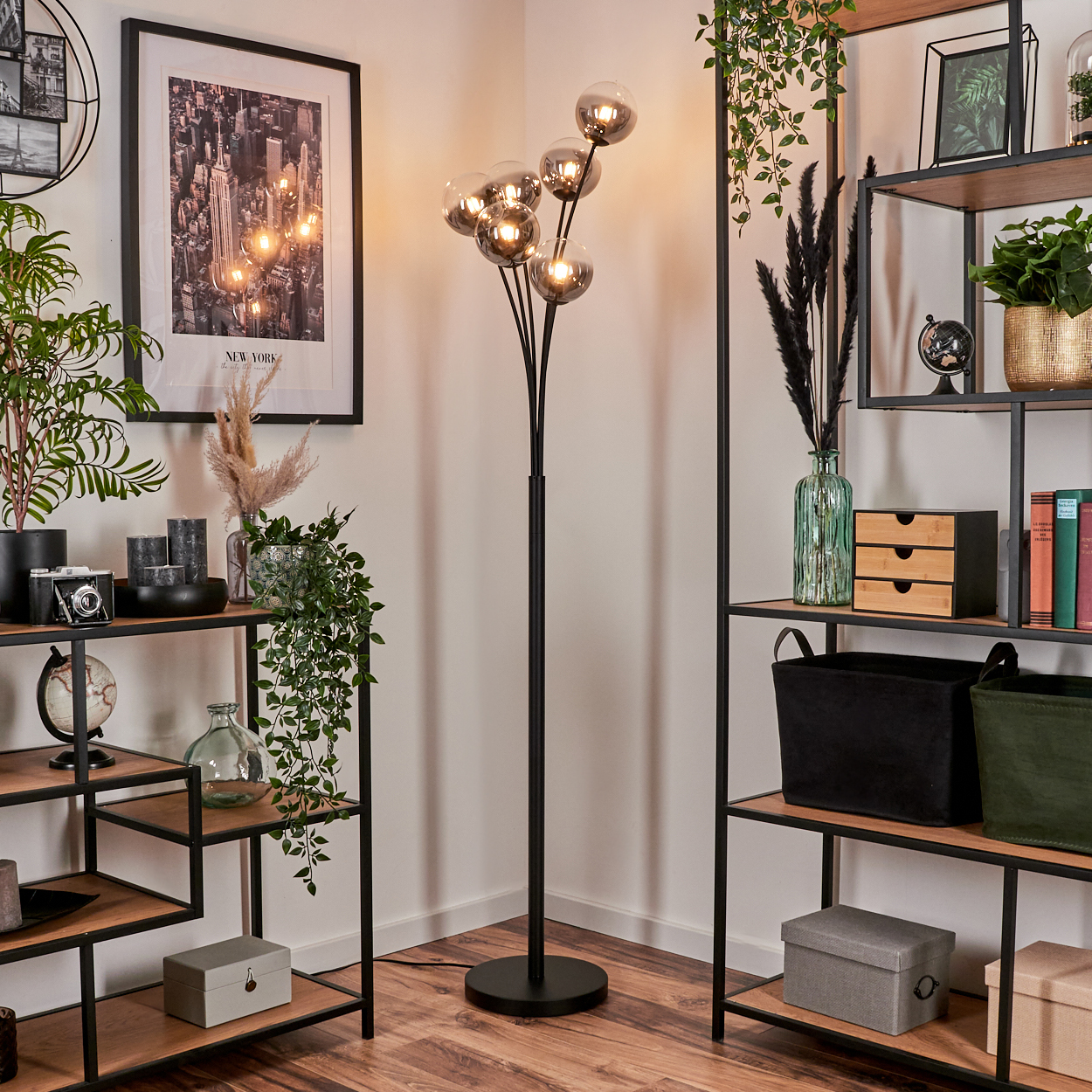 Moderne Stehlampe mit mehreren Glaskugeln, umgeben von Dekoartikeln und Pflanzen.