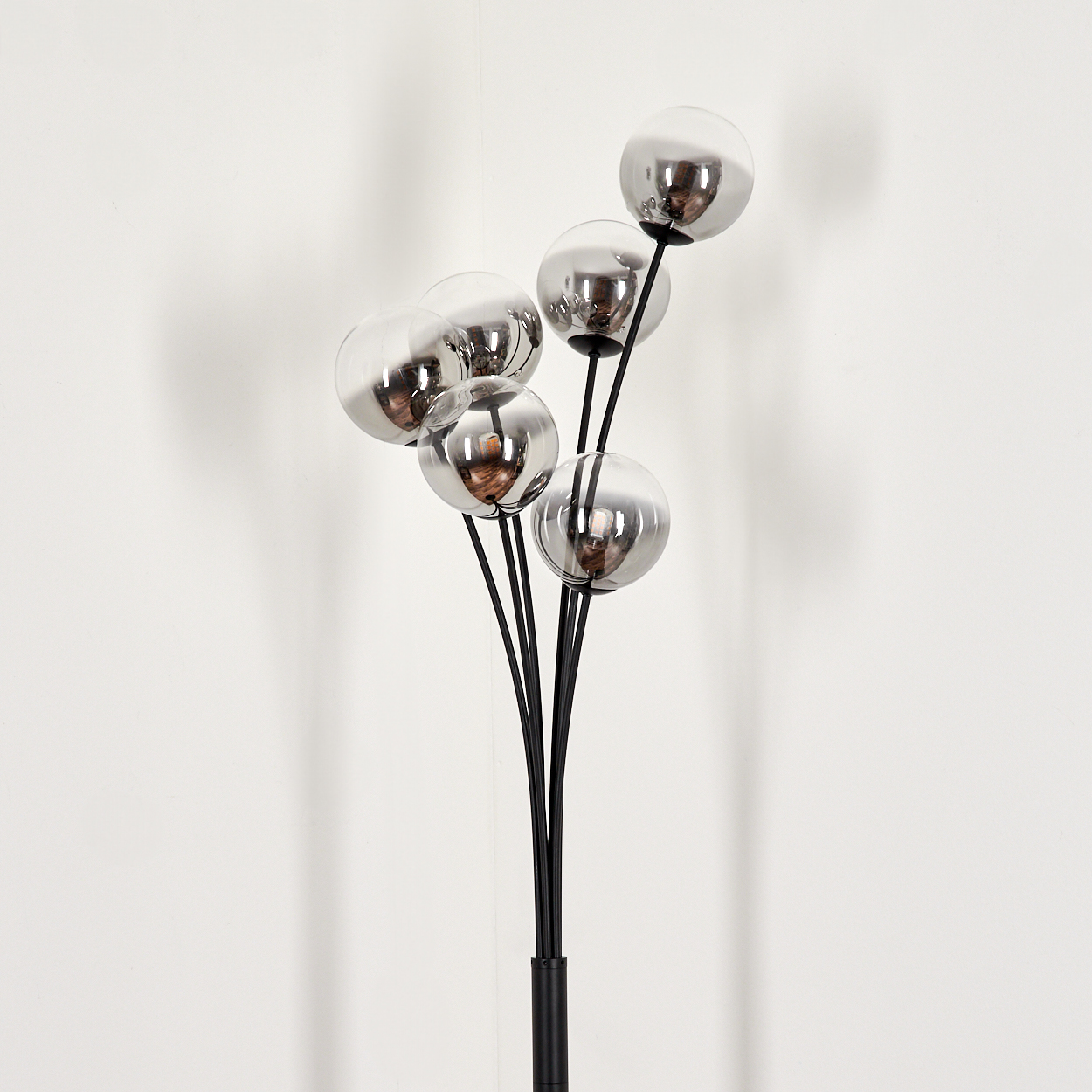 Eine Stehlampe mit sechs grauen Glaskugeln und Glühbirnen vor weißem Hintergrund.
