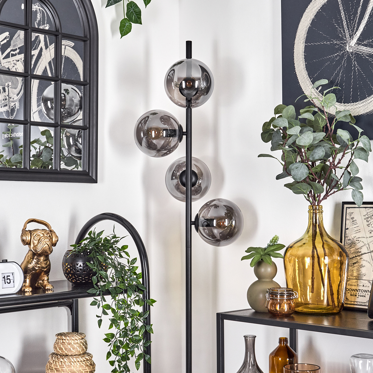 Eine Stehlampe mit vier chromähnlichen Kugeln mit sichtbaren Glühbirnen. Der Hintergrund ist ein Raum.