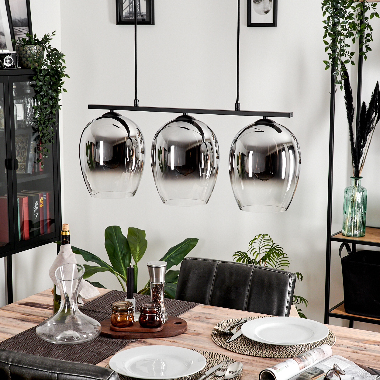 Esszimmer mit drei Pendelleuchten, Dekoration und Esstisch. Hintergrund: Pflanzen und Schrank.