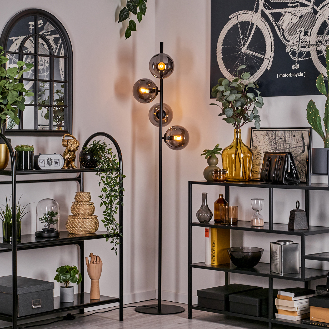 Stehlampe mit vier Glaskugeln, in der Nähe von Regalen mit Deko und einem Fahrradposter an der Wand.