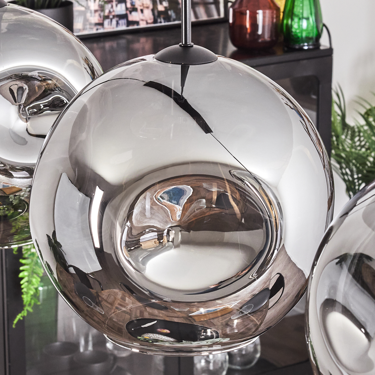Nahaufnahme eines runden, silbernen, wellenförmigen Glasschirms einer Pendelleuchte, der die Umgebung reflektiert.
