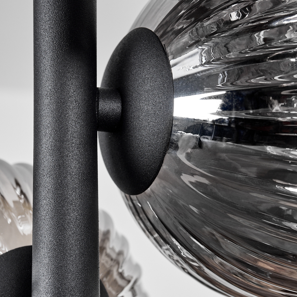 Nahaufnahme einer schwarzen Metallstange und einer silbernen, gerippten Glaskugel, Teil einer Lampe.